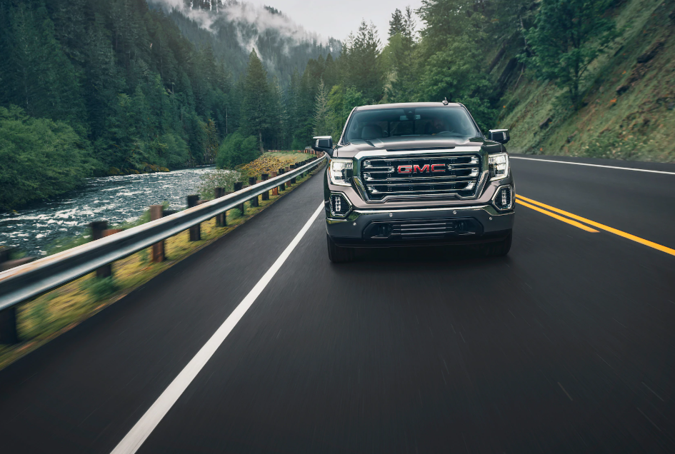 A dark metallic gray colored GMC sierra cruising down a forest road, facing the camera.