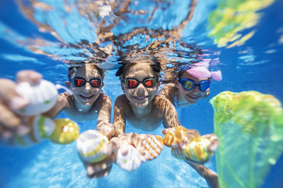Kids wearing goggles underwater in a pool