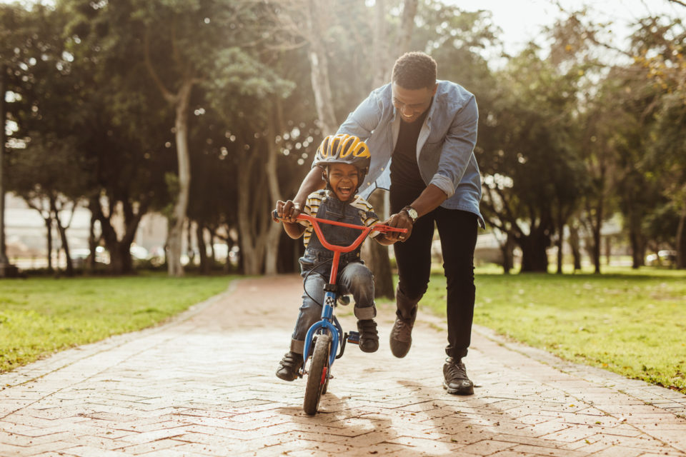 Boy learning to ride a bicycle with his father in park. Father teaching his son cycling at park.