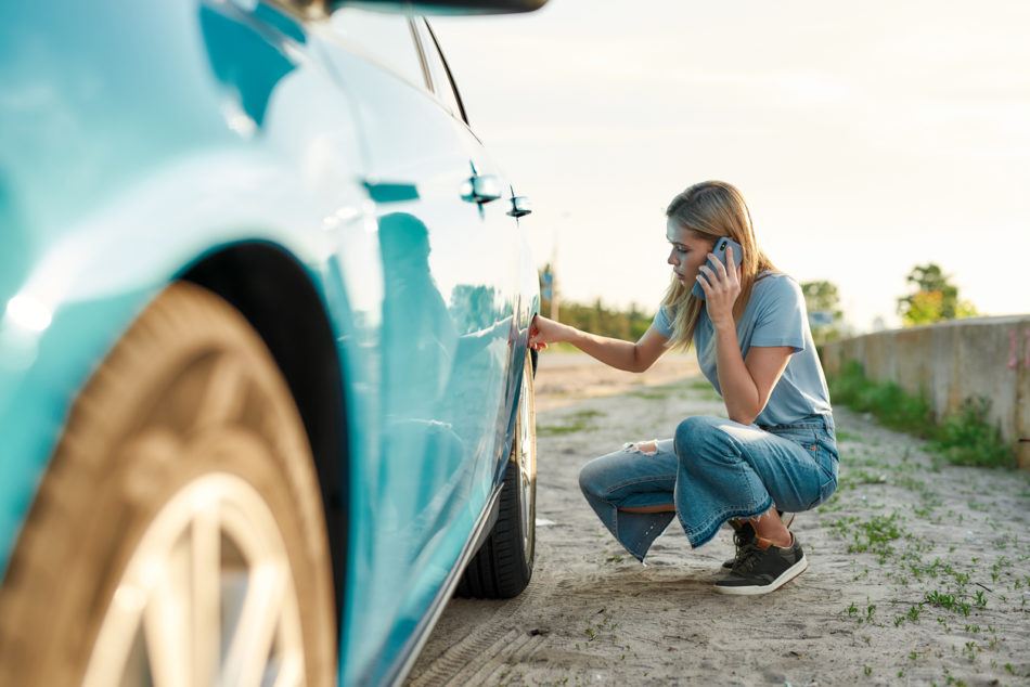 woman looking at tire on the side of the road