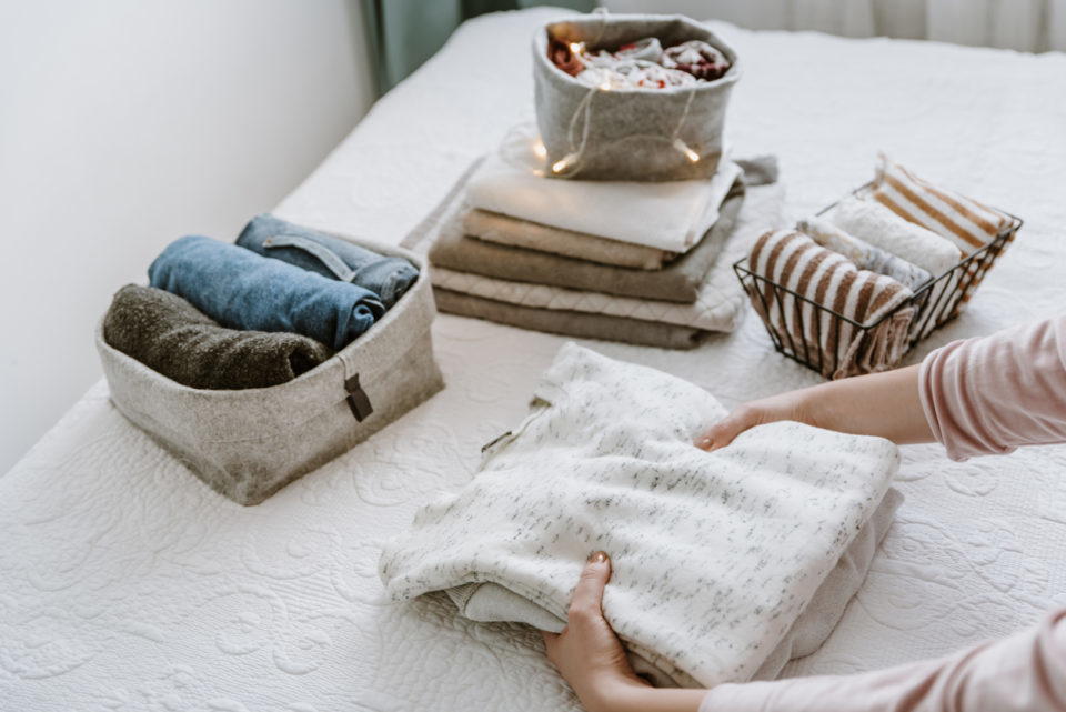 Woman folding stack of fresh laundry, organizing clothes and towels in boxes and baskets.