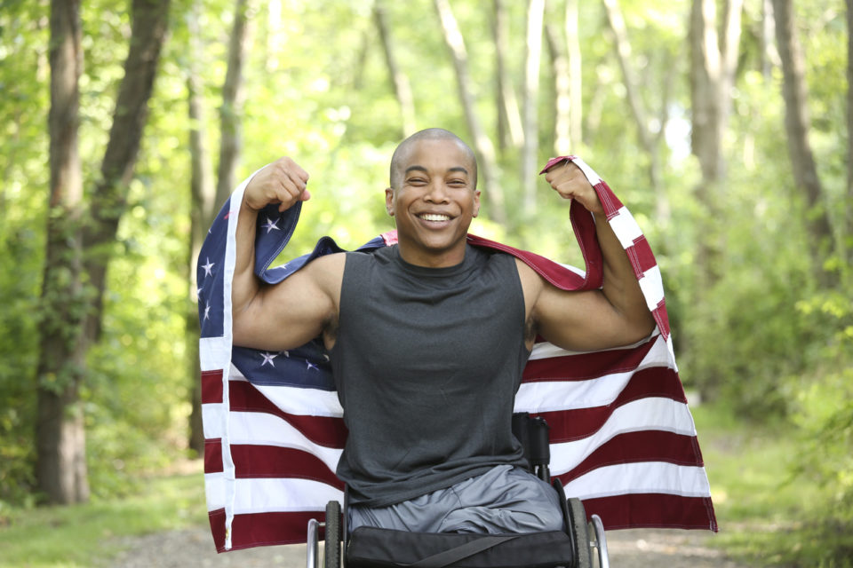 US Veteran in a wheelchair carrying the US Flag.