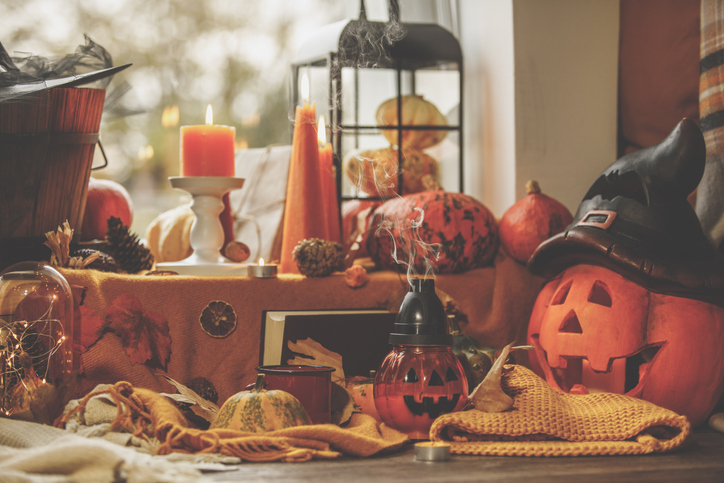 Front view of put out jack-o'-lanterns and pumpkins surrounded by colorful lit candles and Halloween adornments by the window.