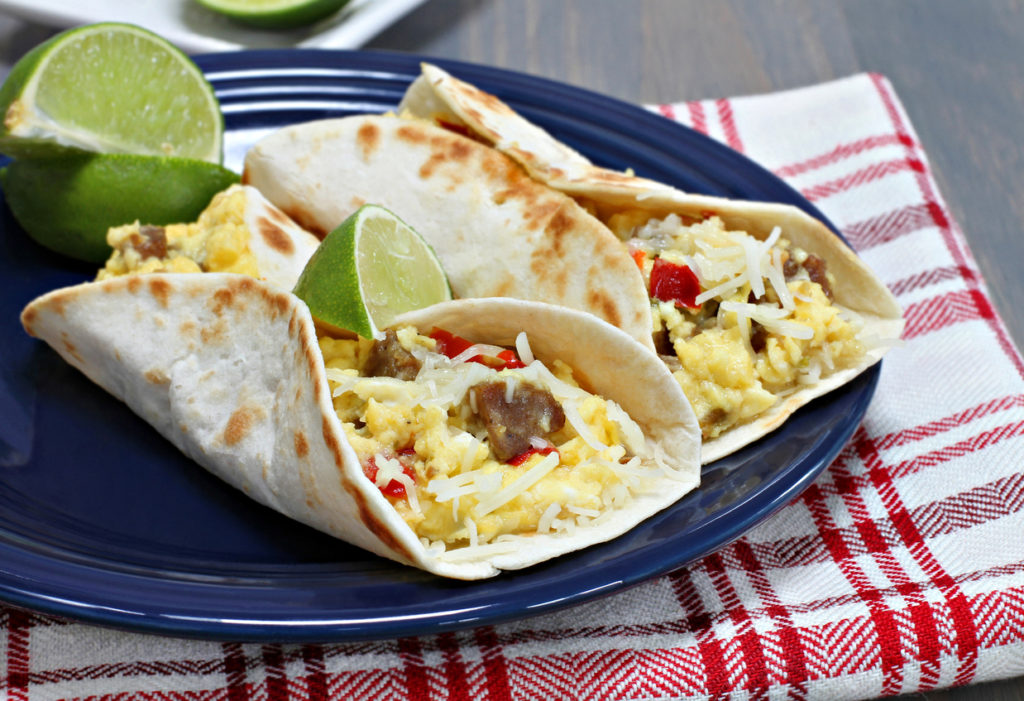 Two breakfast tacos with sausage, cheese, and peppers. Garnished with fresh lime.