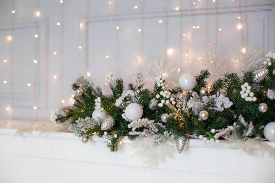 fireplace is decorated with white and silver balls, bells, cones and Christmas tree wreath.