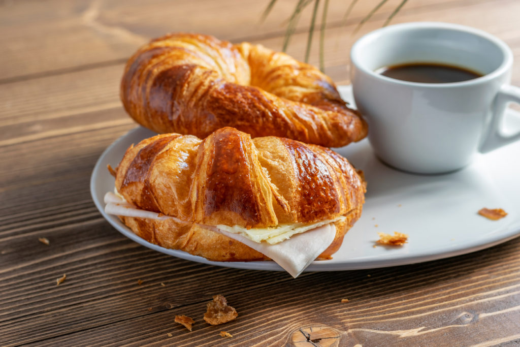 Two French croissants with ham and cheese and a cup of black coffee.