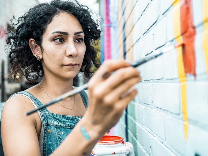 Female artist painting large wall mural.